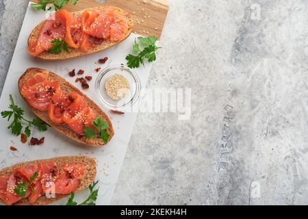 Sandwiches mit gesalzenem Lachs. Offene Sandwiches aus Getreide- oder Vollkorn-Roggenbrot mit gesalzenem Lachs, Sesam und getrockneten Tomaten auf weißem Marmor Stockfoto