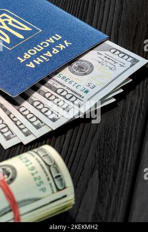 Der ukrainische ausländische biometrische Pass mit Dollars liegt auf schwarzem Holzhintergrund Stockfoto