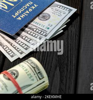 Der ukrainische ausländische biometrische Pass mit Dollars liegt auf schwarzem Holzhintergrund Stockfoto