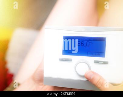 Nahaufnahme einer Frau, die das Drehrad eines angeschlossenen Thermostats mit einer speziellen Meldung auf dem digitalen blauen Punktmatrix-Display dreht - Batterien wechseln - warmes Wetter im Haus des Appartementhauses Stockfoto
