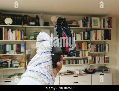 Männliche Hand mit einer bandagierten Hand, die einen Saugpinsel zeigt - moderne Regale im Hintergrund Stockfoto