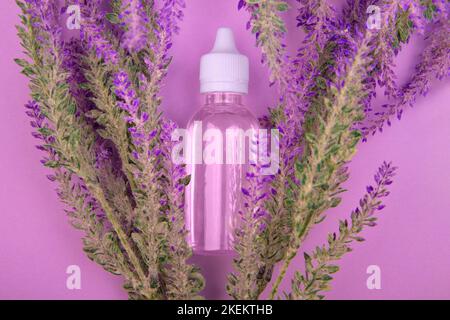 Flüssiger Lavendelextrakt in transparenter Flasche liegt mit Lavendelblüten auf violettem Hintergrund. Draufsicht Stockfoto