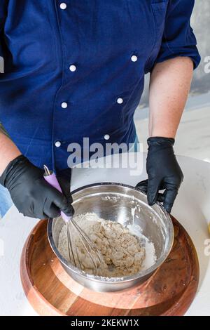 Frau, die Mehl durch ein altes Sieb auf dem Küchenbrett gesiebt hat Stockfoto