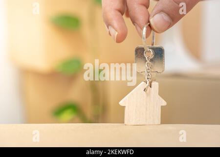 Hand hält Hausschlüssel auf Schlüsselanhänger in der Form eines Holzhauses mit Copy-Space für Text Stockfoto