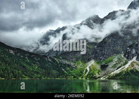 Dramatische Wolken über den Klippen des Rysy-Gebirges, Wald, der sich im Morskie Oko Bergsee im Tatra Nationalpark, Polen, in der Nähe von Zakopane widerspiegelt Stockfoto