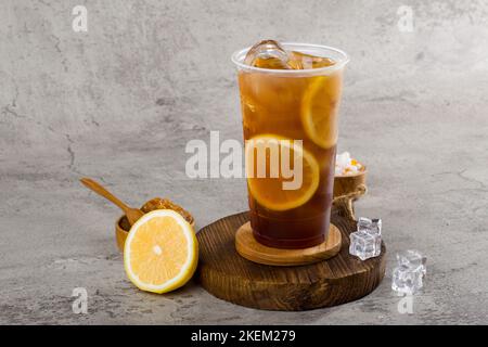 Süßer Limonadentee in Plastikbecher mit Eis auf Texturhintergrund, sommerliche Erfrischung. Stockfoto