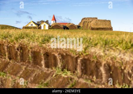 Das Dorf Glumbaer, Island, mit traditionellen Rasenhäusern und einer kleinen rot-weißen Holzkirche. Die Sod Ziegel und Grasdach isoliert Stockfoto