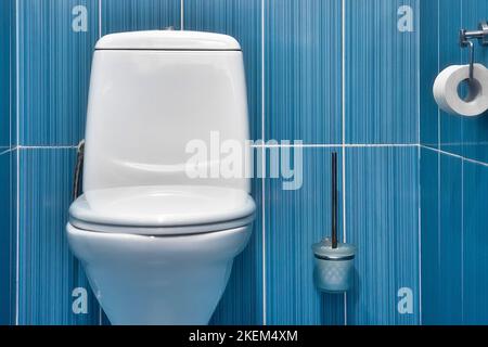 Blick auf weiße Toilette mit geschlossenem Deckel in Toilette mit blau gefliester Wand. Stockfoto