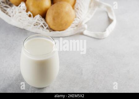 Kartoffelmilch und rohe Kartoffeln in einem Netzbeutel. Alternative Getränke ohne Milchprodukte und Zutaten auf grauem Hintergrund. Allergenfreies und Zero Waste Konzept. Oben Stockfoto