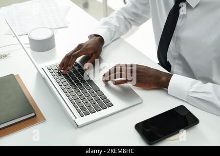 Aus der Perspektive der afroamerikanischen Geschäftsmannes, die während ihrer Arbeit im Büro am Tisch sitzt und auf dem Laptop tippt Stockfoto