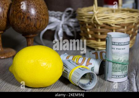 Nahaufnahme von zusammengerollten amerikanischen Dollar-Banknoten und gelber Zitrone auf einem grauen Holztisch. Bank- und Finanzkonzept Stockfoto