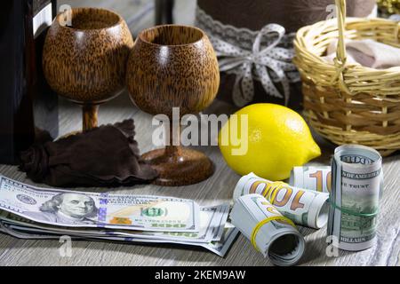 Auf einem grauen Holztisch wurden amerikanische Dollar-Banknoten, Zitrone und zwei Holzkelche zusammengerollt. Bank- und Finanzkonzept Stockfoto