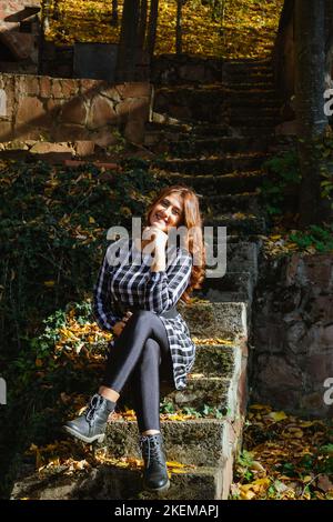 Farbenfrohe Herbstlandschaft mit einem hübschen jungen Mädchen im Kleid, das auf der Treppe sitzt. Reisen und Abenteuer in Serbien. Stockfoto