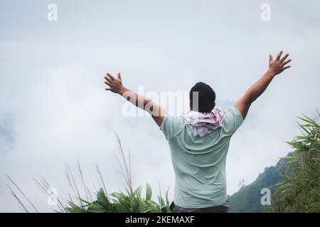 Ein Bergsteiger steht mit ausgestreckten Armen auf einem nebligen hohen Berg, um Erfolg und Freiheit zu vermitteln Stockfoto