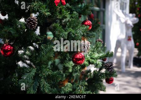 Geschlossener Weihnachtsbaum, geschmückt mit Ornamenten, roten Kugeln und Tannenzapfen, die am Baum hängen. Stockfoto