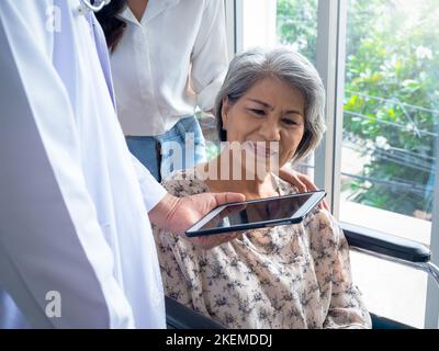 Porträt einer lächelnden älteren Frau Patienten im Rollstuhl mit Assistent nehmen sie zu einem Arzt mit, der eine Tablette verwendet und ihre medizinische Behandlungsakte diskutiert Stockfoto