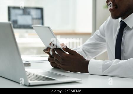 Nahaufnahme eines afroamerikanischen Geschäftsmannes, der bei seiner Arbeit ein digitales Tablet benutzte, während er am Tisch im Büro saß Stockfoto