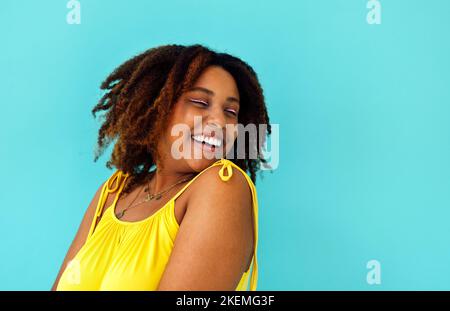 Schöne helle fröhliche afrikanische Frau in gelbem Kleid im blauen Studio-Hintergrund Stockfoto