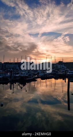 Ein mezmerisierender Blick auf verschiedene Boote und den Hafen bei einem wunderschönen Sonnenuntergang, der sich im Wasser widerspiegelt Stockfoto