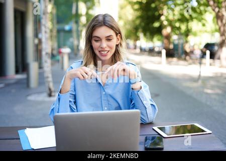 Junge Geschäftsfrau, nehmen an einer Online-Videokonferenz Teil, schreiben, arbeiten, Notizen in ihren Dokumenten machen, draußen an der frischen Luft sitzen Stockfoto