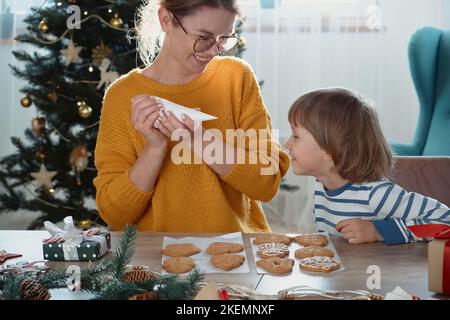 Mutter und Kind dekorieren Weihnachts-Lebkuchenkekse mit Zuckerguss und haben Spaß zusammen Stockfoto