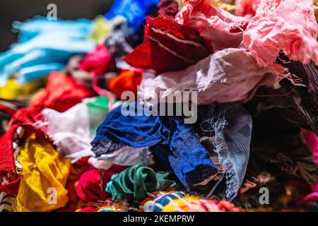 Ein Stapel mehrfarbiger synthetischer Stoffe mit unterschiedlichen Strukturen und Texturen. Ein Stapel von bunten Stoffen glatte Formen Hintergrund. Nahaufnahme Stockfoto