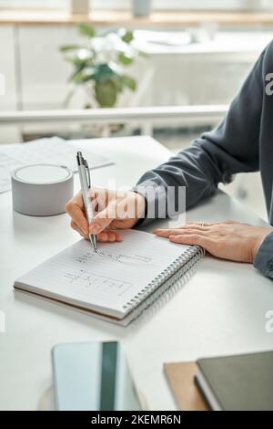 Nahaufnahme der Managerin, die an ihrem Arbeitsplatz im Büro arbeitet, und sie schreibt Finanzdiagramme in Notizblock Stockfoto