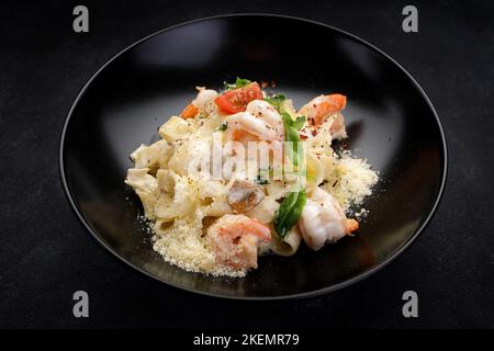 Pasta mit Garnelen, Käse, Pilzen und Gemüse auf dunklem Hintergrund Stockfoto