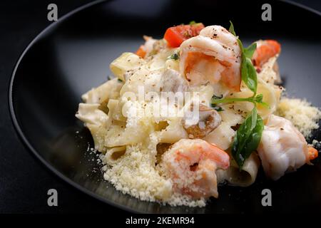 Pasta mit Garnelen, Käse, Pilzen und Gemüse auf dunklem Hintergrund Stockfoto