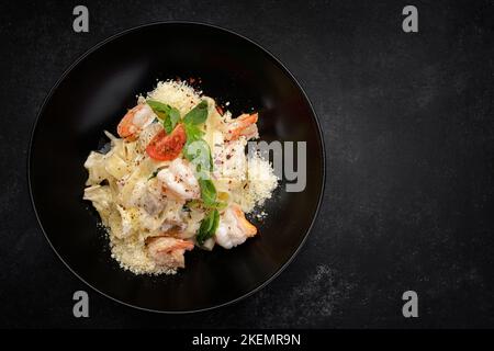 Pasta mit Garnelen, Käse, Pilzen und Gemüse auf dunklem Hintergrund Stockfoto