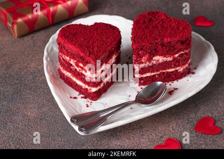 Zwei Kuchen Roter Samt in Herzform auf weißem Teller und Geschenke auf braunem Hintergrund, Kuchen zum Valentinstag Stockfoto