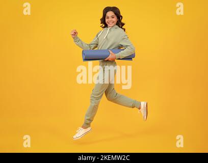 Sportbekleidung Werbekonzept. Laufen und springen. Teenager Kind Mädchen in Trainingsanzügen Jogginganzug posiert im Studio halten Fitness-Matte. Stockfoto