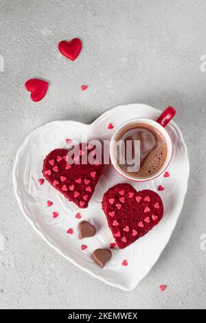 Kuchen Roter Samt in Herzform auf weißem Teller und Tasse Kaffee zum Valentinstag auf hellgrauem Hintergrund, Draufsicht Stockfoto