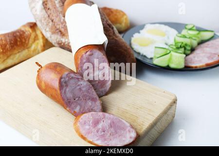 Stillleben aus Schinkenwurst in einem Laib auf einem Holztablett. Ein Laib Wurst und Stückchen Wurst aus der Nahaufnahme. Fleischfutter. Stockfoto