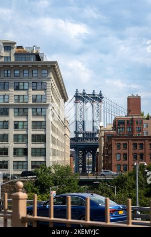 Manhattan Bridge zwischen Manhattan und Brooklyn über dem East River von einer schmalen Straße aus gesehen, die an sonnigen Tagen in New York von Gebäuden umgeben ist Stockfoto