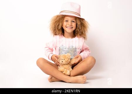 Kleines Mädchen trägt Strohhut umarmt Teddybär isoliert auf weißem Hintergrund. Stockfoto