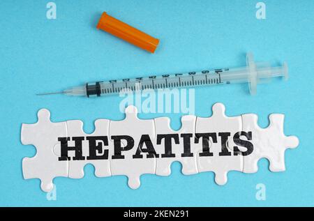 Medizinkonzept. Auf blauem Hintergrund eine Spritze und Puzzles mit der Aufschrift - Hepatitis Stockfoto