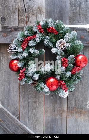 Weihnachtskranz aus Fichtenzweigen aus glasroten Kugeln, die am Holzzaun des Dorfhauses hängen Stockfoto