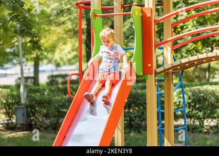 Aktives Kind auf farbenfroher Rutsche. Kinder spielen auf dem Spielplatz im Freien Stockfoto