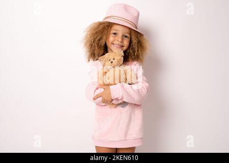 Kleines Mädchen trägt Strohhut umarmt Teddybär isoliert auf weißem Hintergrund. Stockfoto