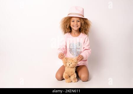 Kleines Mädchen trägt Strohhut umarmt Teddybär isoliert auf weißem Hintergrund. Stockfoto