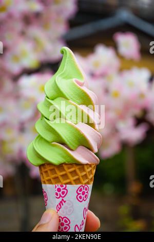 Eine vertikale Aufnahme eines grün-rosa Eiskegels auf einem Hintergrund blühender Blumen Stockfoto