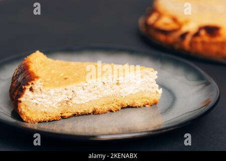 Hausgemachter Käsekuchen auf einem grauen Teller auf schwarzem Tisch, Nahaufnahme. Stockfoto