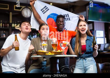 Eine Gruppe glücklicher Fans feiert den Sieg ihrer Lieblingsmannschaft mit der Flagge Südkoreas in der Bierstube Stockfoto