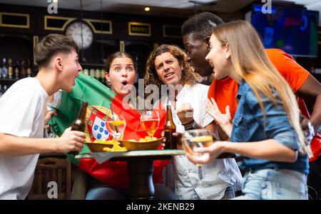 Begeisterte diverse Fußballfans mit Flagge Portugals mit einem Pint Bier und Chips im Pub Stockfoto