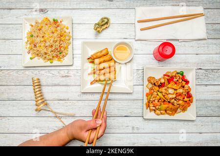 Die Hand hält Holzstäbchen, um vietnamesische Brötchen zu essen, drei erfreuen Reis und Huhn mit Mandeln Stockfoto