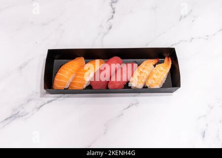 Schwarzes Liefertablett mit sechs Nigiri-Sushi verschiedener Fische Stockfoto