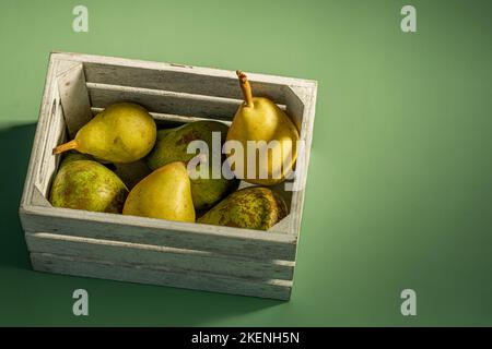 Holzkiste voller reifer Birnen verschiedener Sorten auf schlichtem grünen Hintergrund Stockfoto