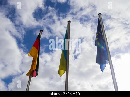 Die Flaggen der Ukraine, Deutschlands und der Europäischen Union fliegen Seite an Seite gegen den blauen Himmel Stockfoto