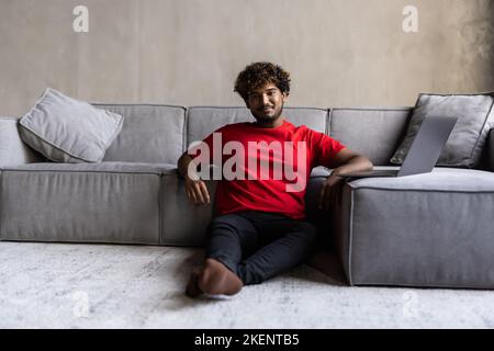 Junger, hübscher inder, der im Wohnzimmer auf einem Laptop sitzt Stockfoto